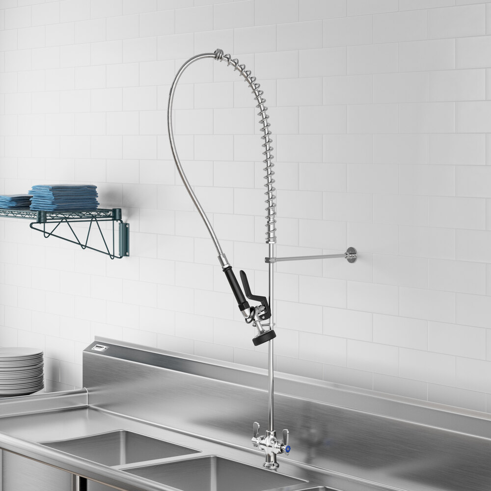 A commercial-style pre-rinse faucet with a flexible hose and spray nozzle mounted above a stainless steel sink in a kitchen setting.
