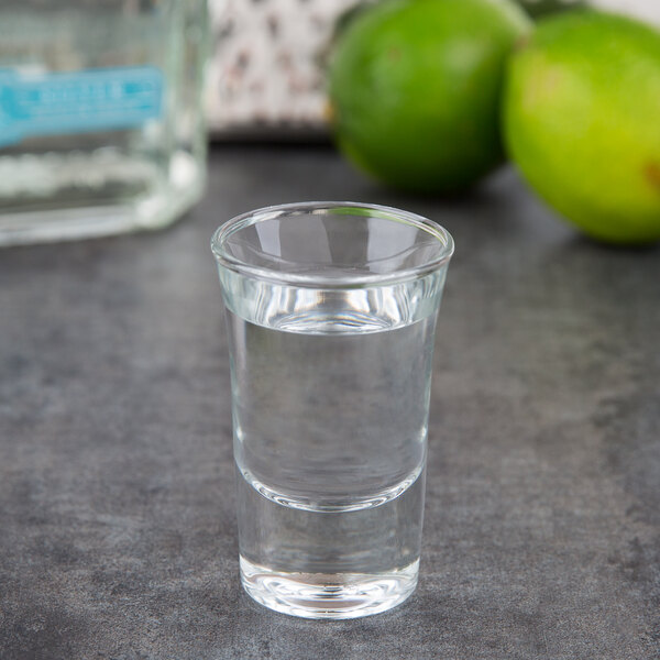 An Arcoroc tall shot glass filled with clear liquid and a lime slice.