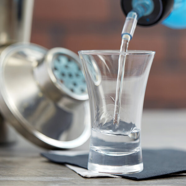 A close-up of clear liquid being poured into an Arcoroc shot glass.