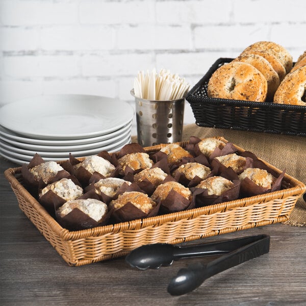 A honey rectangular plastic basket filled with bread and muffins on a table.
