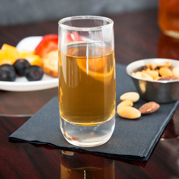 A Arcoroc Cabernet cordial glass filled with brown liquid on a table with a bowl of nuts.