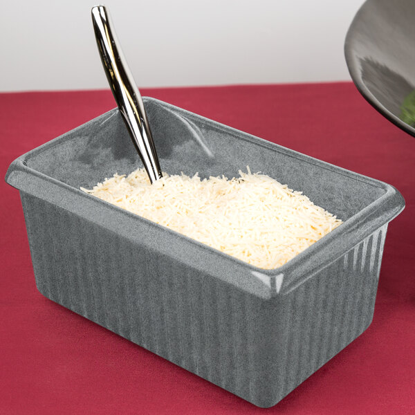 A Tablecraft granite rectangle server with a spoon in a container with shredded cheese.