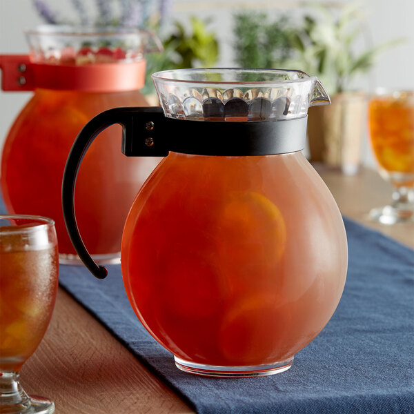 A clear plastic pitcher with a black handle filled with orange liquid and a glass of orange liquid.