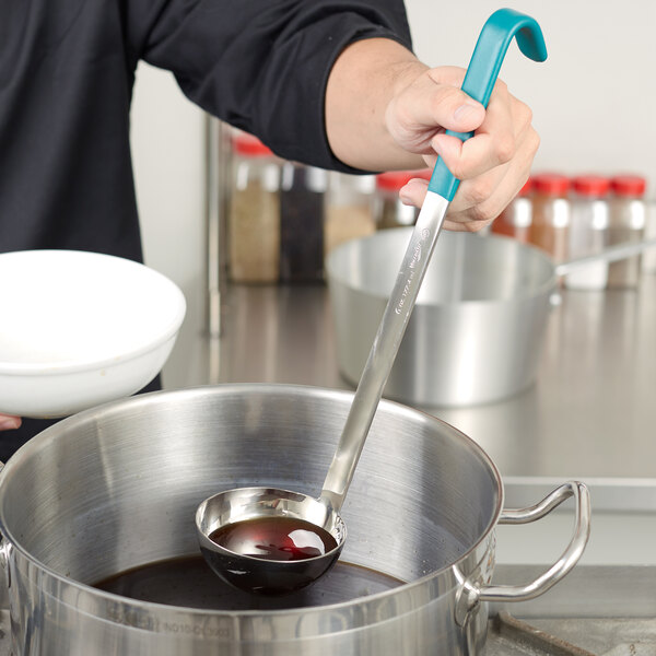 A person using a Vollrath ladle with a teal handle to stir brown liquid in a white bowl.