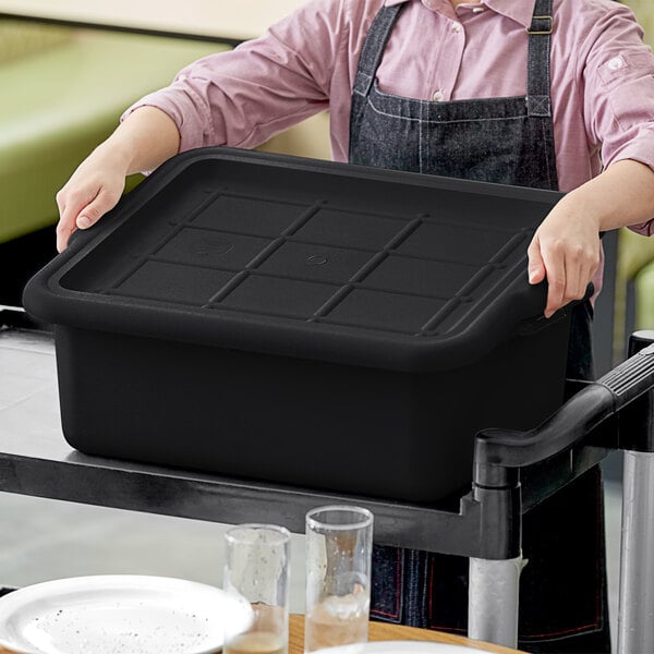 A woman holding a Tablecraft black rectangular bus tub cover on a tray.