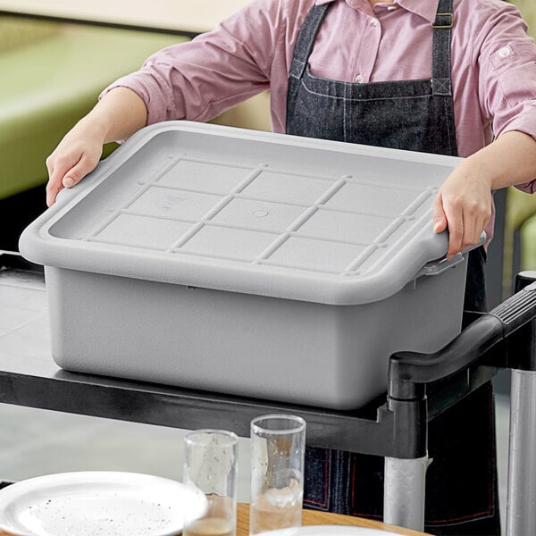 A woman holding a Tablecraft grey plastic bus tub cover on a tray.