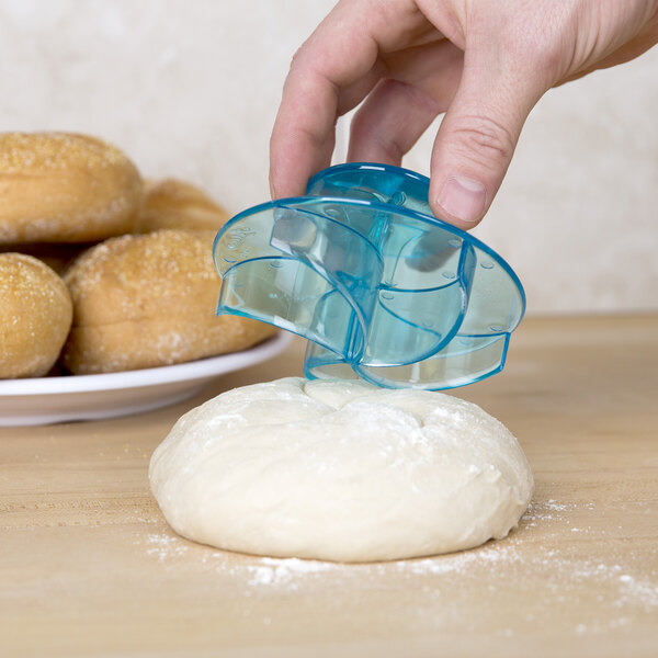 A person using an Ateco Kaiser roll stamp to cut dough.