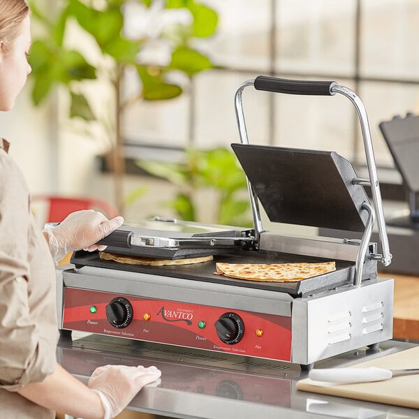 A woman cooking food on an Avantco commercial panini grill.