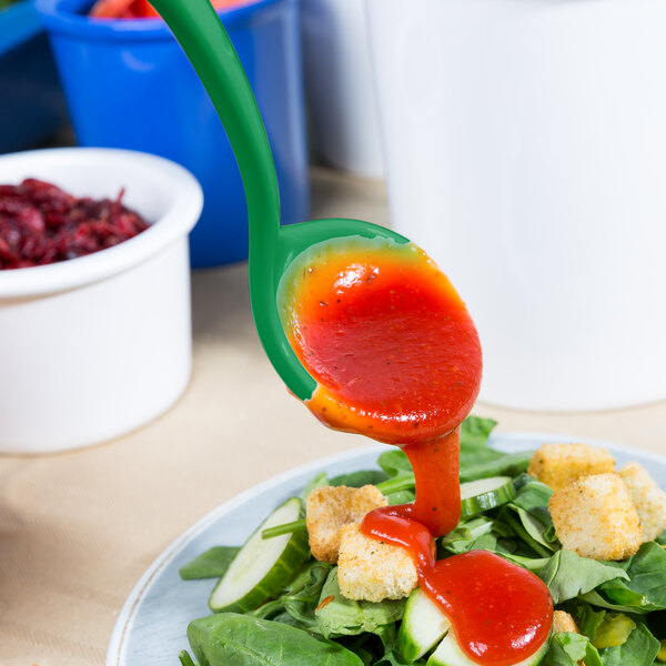 A green Tablecraft long ladle pouring sauce onto a salad.