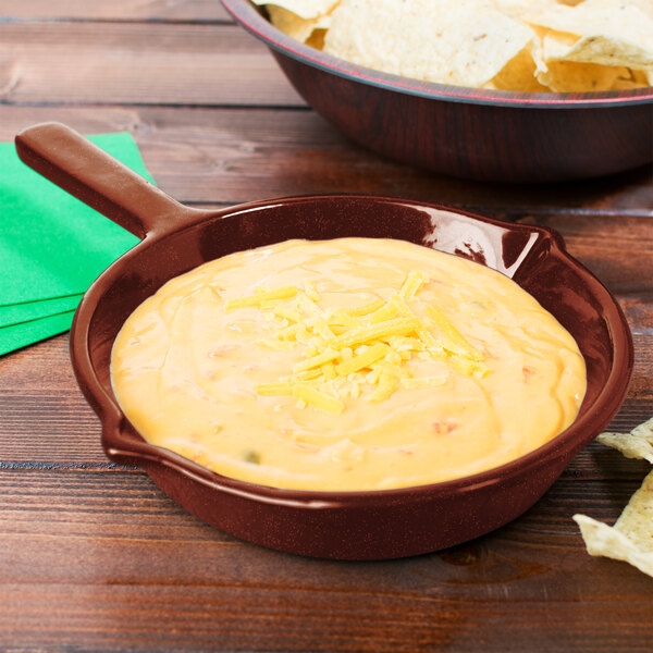 A maroon speckled fry pan with a bowl of cheese dip next to a bowl of chips.