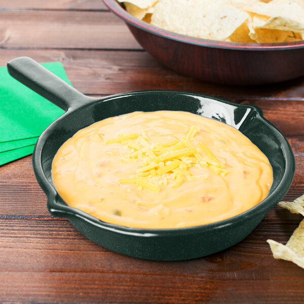 A Tablecraft hunter green and white speckled fry pan filled with cheese dip next to a bowl of chips on a table.