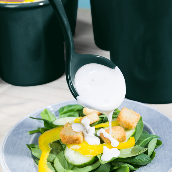 A Tablecraft hunter green cast aluminum ladle pouring dressing over a salad.