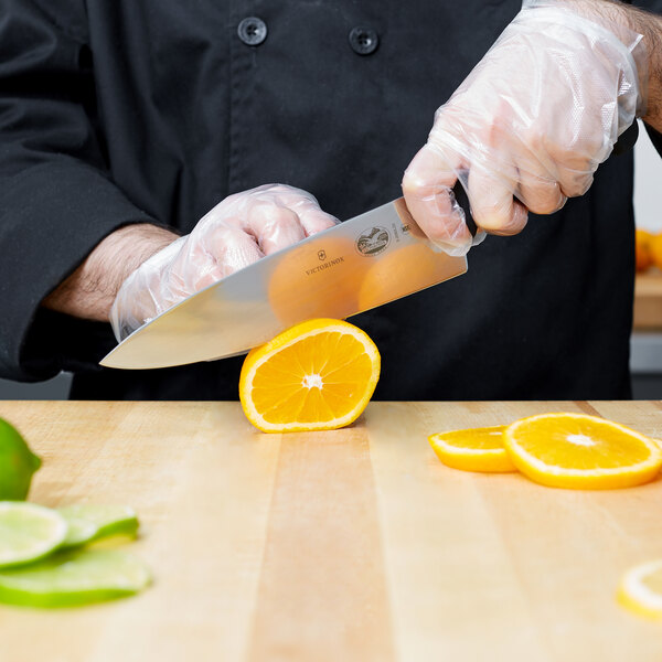 A person using a Victorinox chef knife to slice an orange.