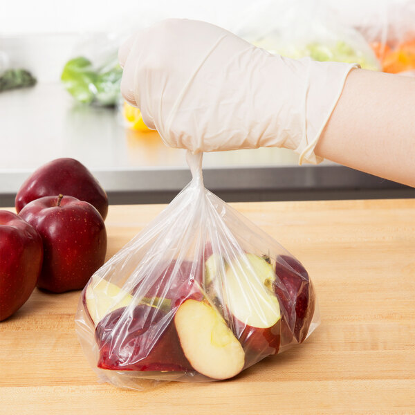 A person wearing a glove holding a plastic bag of red apples.
