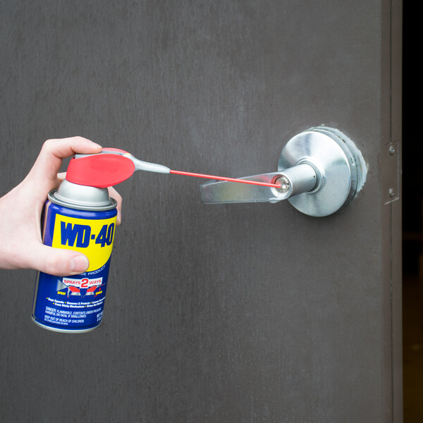 A person using WD-40 spray lubricant with Smart Straw on a door.