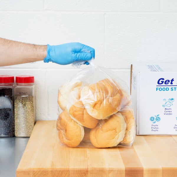 A gloved hand holding a plastic bag of bread.