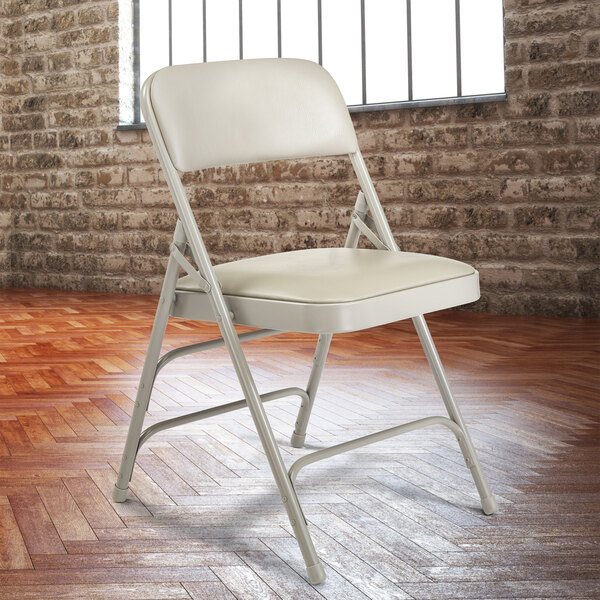 A gray metal folding chair with a warm gray padded seat in front of a brick wall.