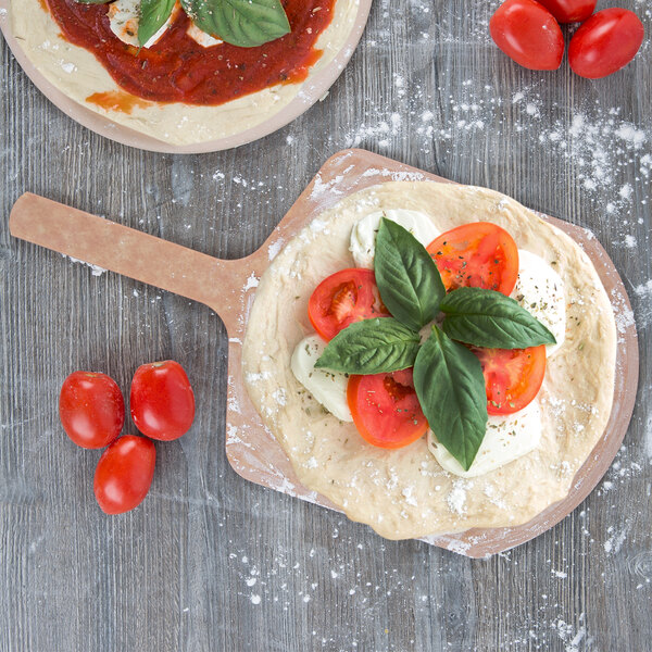 A pizza with tomatoes and basil on a pizza peel.