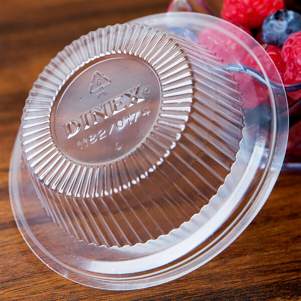 A plastic container with a Dinex clear lid and berries on a wood surface.