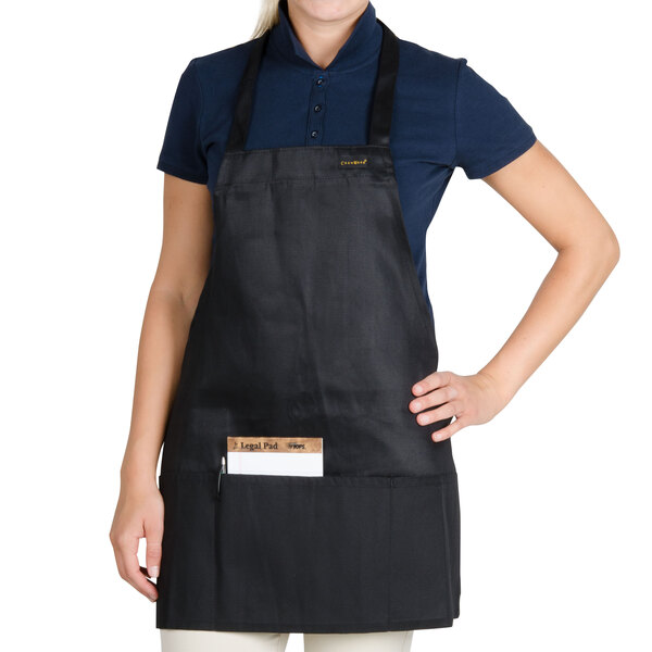 A woman wearing a black Chef Revival bib apron with one pocket.