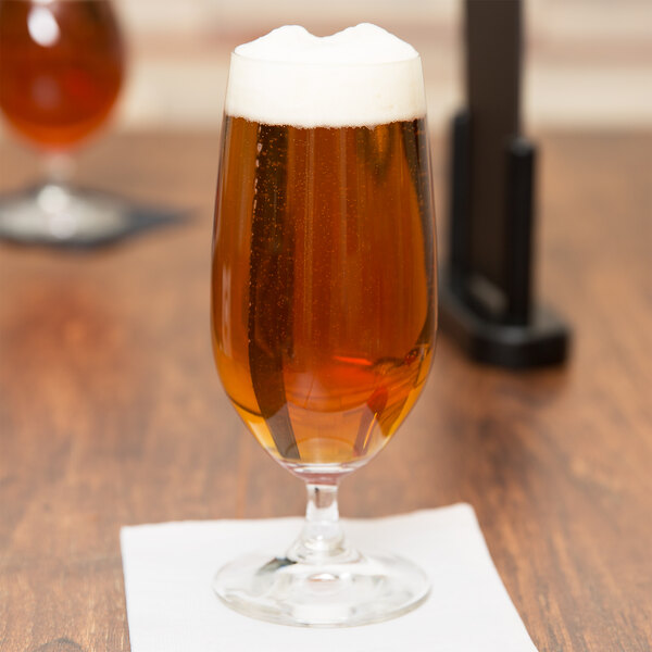 A Spiegelau Vino Grande stemmed Pilsner glass full of beer on a table with a napkin.