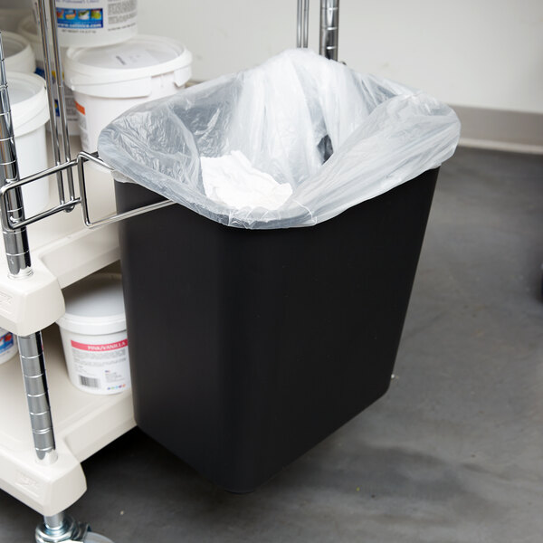 A black Metro wastebasket attached to a Metro cart with a plastic bag inside.