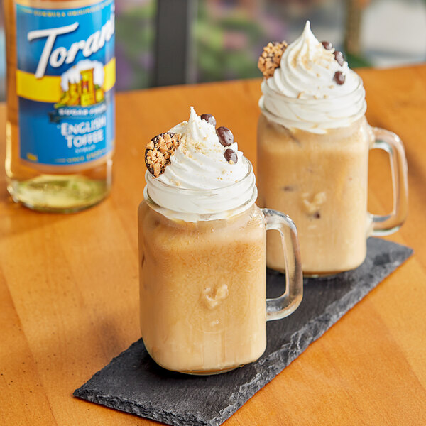 A glass mug of Torani Sugar-Free English Toffee flavoring syrup in a coffee drink with whipped cream and chocolate chips.