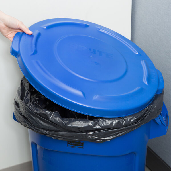 A hand placing a blue lid on a Rubbermaid blue garbage can.