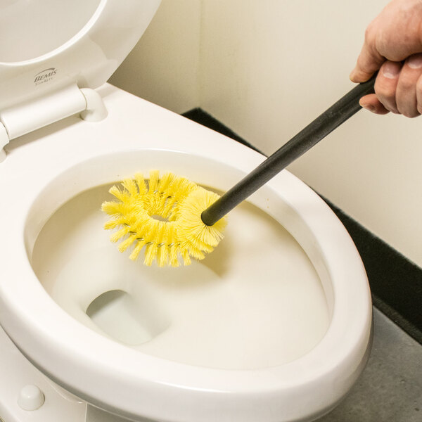 A person using a Carlisle black toilet bowl brush to clean a toilet.