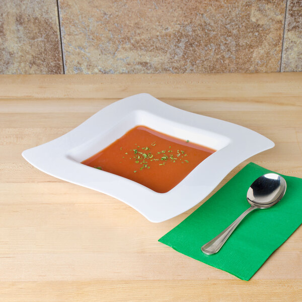 A white Fineline disposable plastic bowl of soup on a table with a spoon.