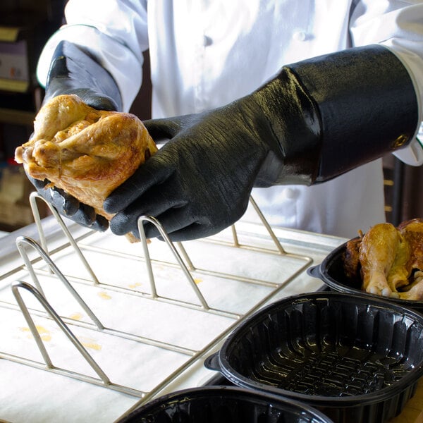 A person wearing San Jamar elbow-length black neoprene gloves holding a cooked chicken.