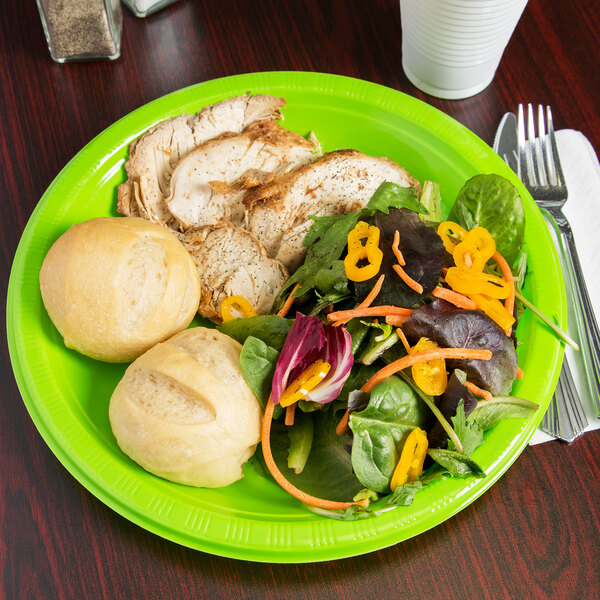 A Creative Converting Fresh Lime green plastic plate with a salad and bread on a table.