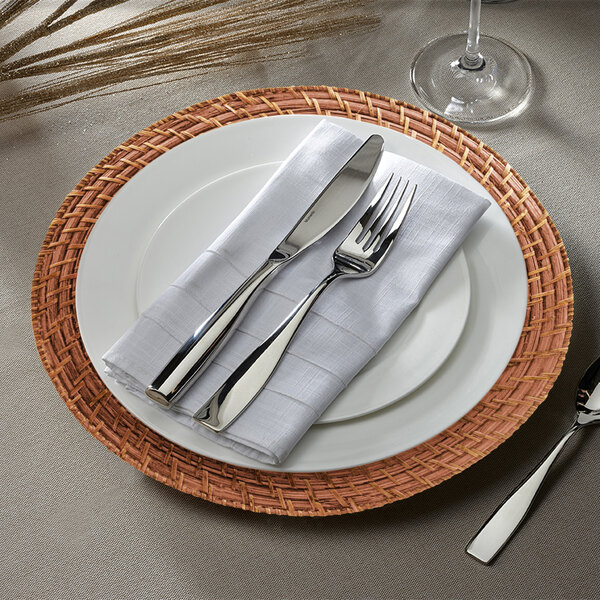 A round amber rattan charger plate with silverware and a white napkin on it.