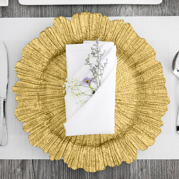 A folded napkin on a Charge It by Jay Reef Gold charger plate with purple and white flowers.