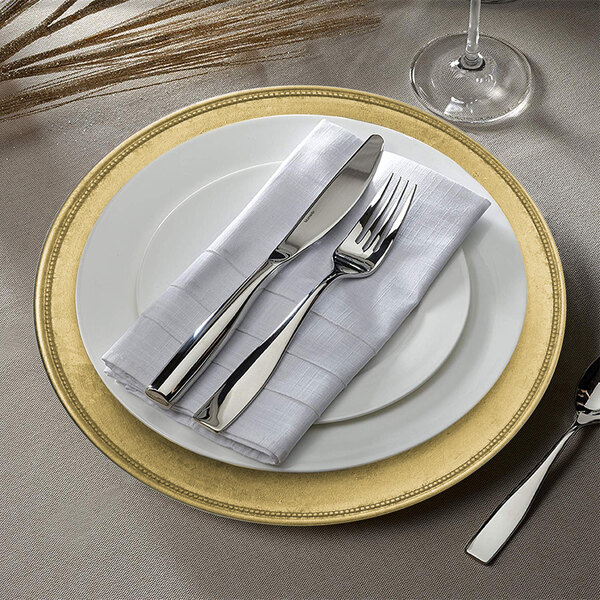 A white plastic charger plate with a gold rim and silverware on it.