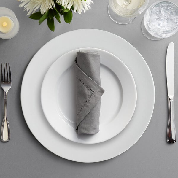 A white Charge It by Jay plastic charger plate with silverware and a napkin on a table.