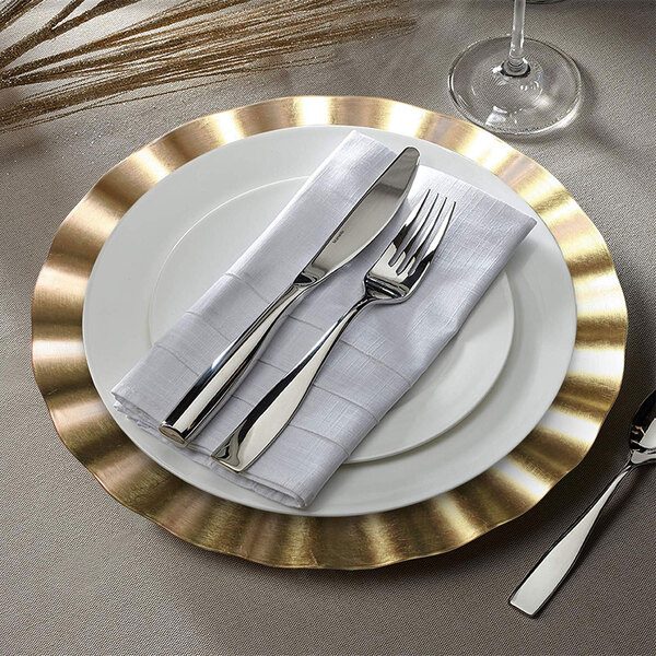 A white plate with a gold ruffled rim and silverware on it.