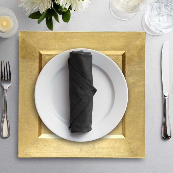 A gold plastic charger plate with a napkin, fork, and knife on it.