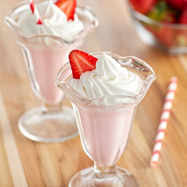 Two glasses of pink Big Train Strawberry Frappes with whipped cream and strawberries.
