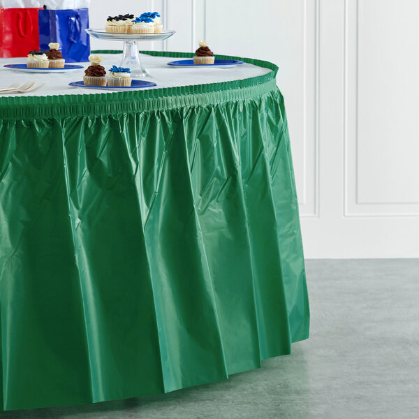 A table with an emerald green plastic table skirt over a white tablecloth.