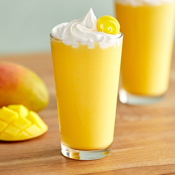 A glass of yellow Big Train mango frappe with whipped cream and mango.