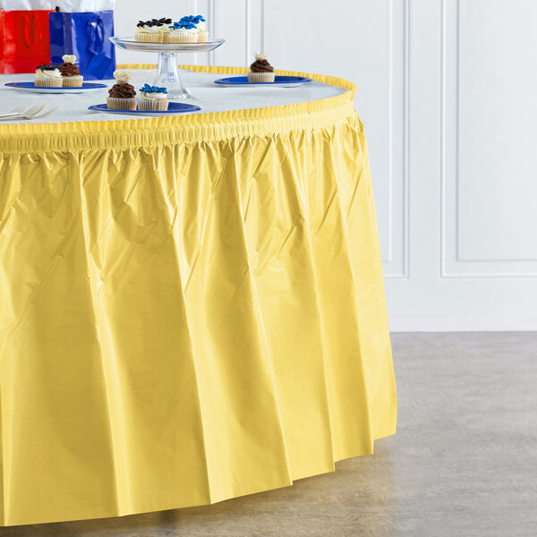 A yellow Creative Converting disposable table skirt on a table with a yellow tablecloth.