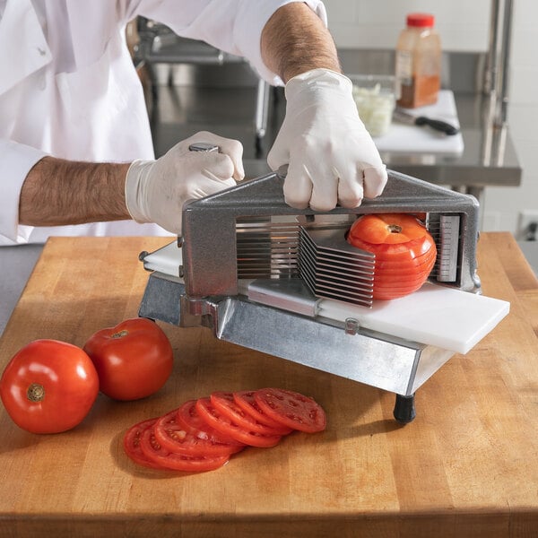 A person using a Nemco Easy Tomato Slicer to slice tomatoes on a cutting board.