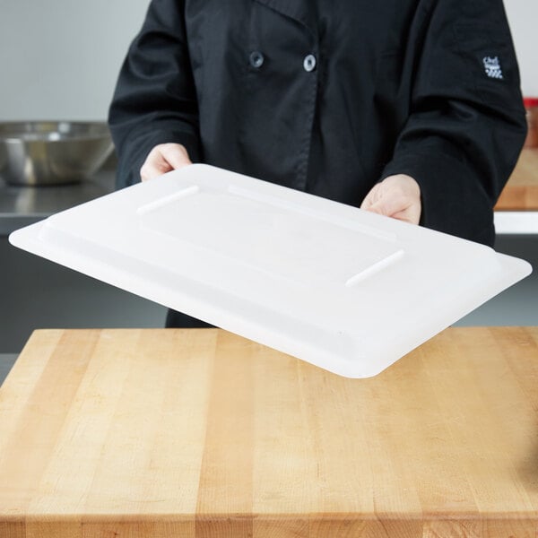 A person holding a Carlisle white plastic food storage lid over a large white plastic container on a counter.