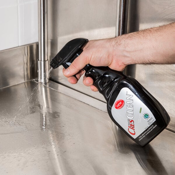 A hand using a spray bottle to clean a stainless steel sink.