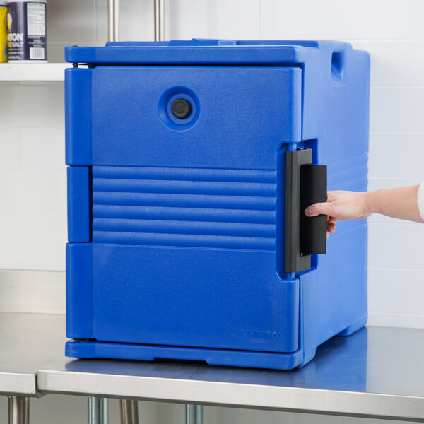 A hand opening the front of a navy blue Cambro Ultra Pan Carrier on a counter.