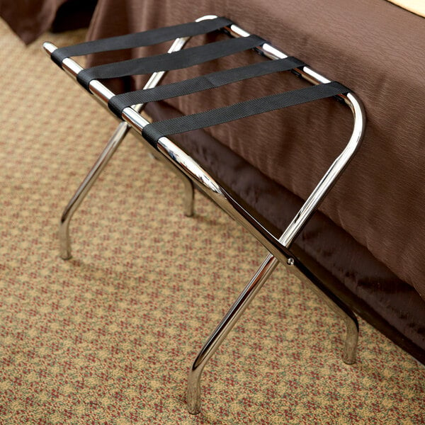 A Lancaster Table & Seating chrome folding luggage rack with straps on it.