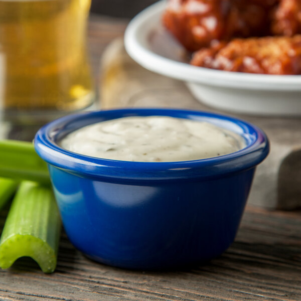 A blue bowl of white sauce next to celery sticks and chicken wings.