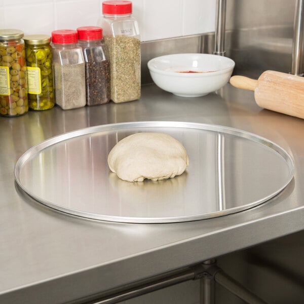 Pizza dough on an American Metalcraft aluminum pizza pan on a counter.