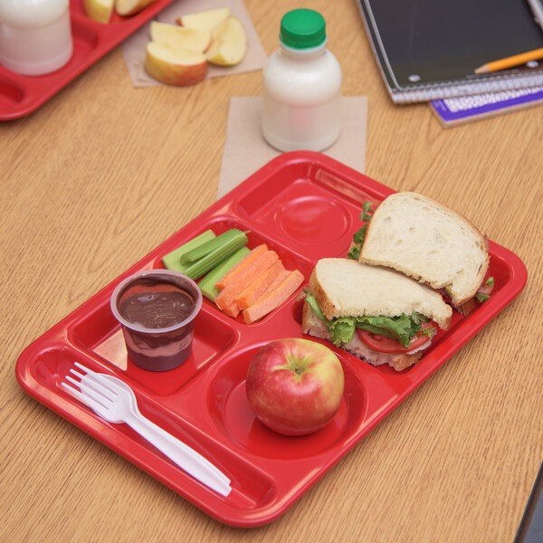 A Carlisle red school lunch tray with a sandwich, vegetables, and a drink.